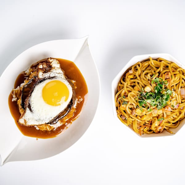 Hawaiian Loco Moco with a fried egg and gravy, alongside a bowl of noodles with corn and sprouts.