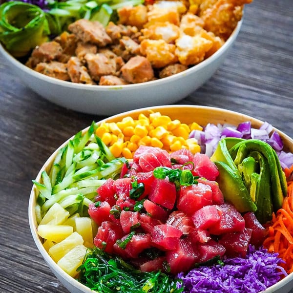 Two colorful Hawaiian poke bowls, one with tuna, avocado, and corn, the other with chicken.