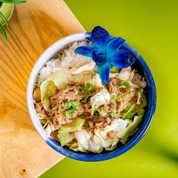 A Hawaiian kalua pig and cabbage bowl with rice, garnished with a blue orchid.