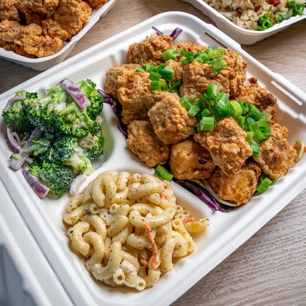 Hawaiian fried chicken with green onions, macaroni salad, and broccoli salad in a takeout container.