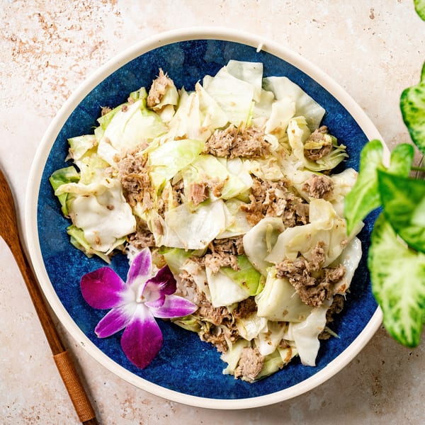 Hawaiian-style cabbage and pork dish, garnished with a purple orchid, in a blue bowl.