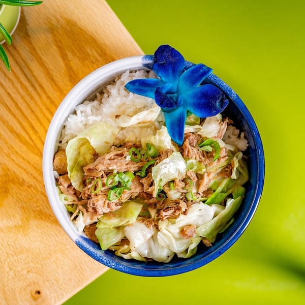 Hawaiian Kalua Pork and Cabbage bowl with rice, garnished with a blue orchid.
