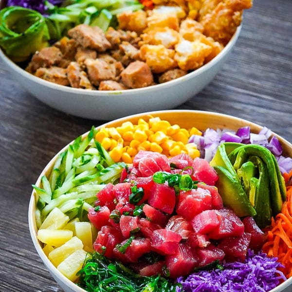 Two vibrant Hawaiian poké bowls, one with tuna, avocado, and corn, the other with chicken.