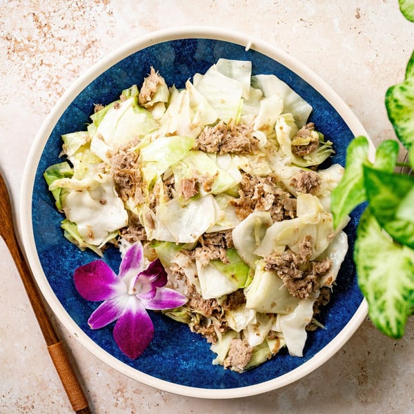 Hawaiian cabbage and tuna dish in a blue bowl with an orchid, on a textured surface.