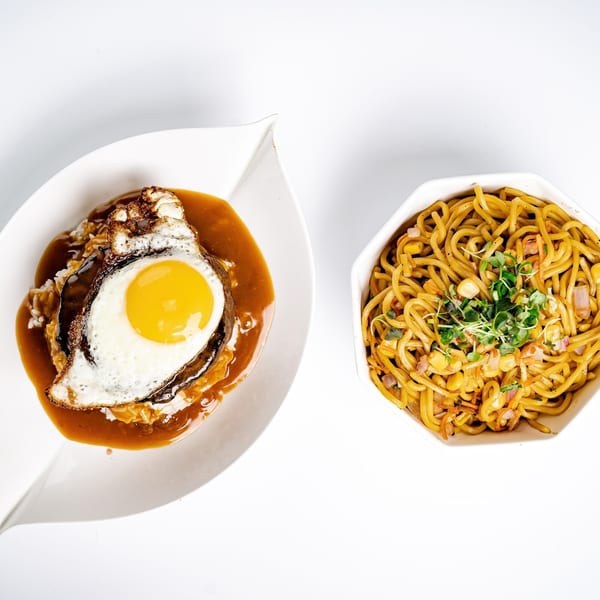 Hawaiian Loco Moco with a fried egg and gravy, next to a bowl of noodles with corn and sprouts.