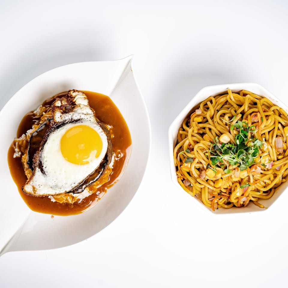 Hawaiian Loco Moco with a fried egg and gravy, next to a bowl of noodles with corn and sprouts.